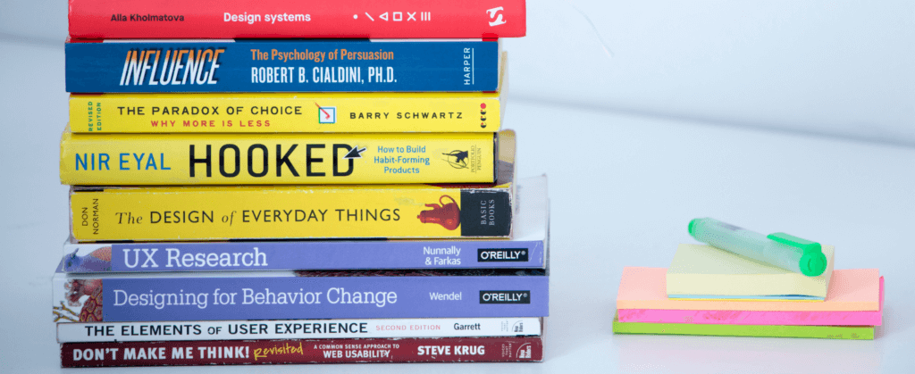 A stack of UX books next to post-its and a pen